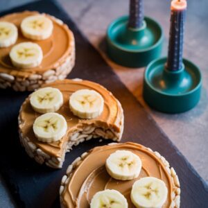 Low FODMAP peanut butter banana rice cakes on slate with candlelight, showing safe banana portion and creamy peanut butter texture.
