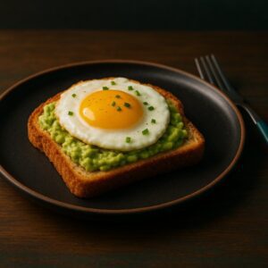 Low FODMAP avocado egg toast: a matte-black plate on a rustic walnut tabletop holding a slice of toasted low-FODMAP bread topped with mashed avocado and a perfectly cooked egg, garnished with chopped chives, under warm side lighting and subtle teal-fill.